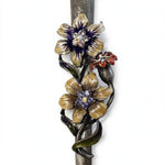 Wildflower Garden Pewter Mezuzah shown from the front as a mezuzah cover featuring yellow and purple flowers with sparkling centers, a small reddish blossom and green curling leaves along a textured silver-toned pewter stem, presenting a detailed Judaica design for a Jewish home doorway