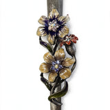 Wildflower Garden Pewter Mezuzah shown from the front as a mezuzah cover featuring yellow and purple flowers with sparkling centers, a small reddish blossom and green curling leaves along a textured silver-toned pewter stem, presenting a detailed Judaica design for a Jewish home doorway