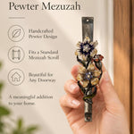 Handheld portrait of the Wildflower Garden Pewter Mezuzah mezuzah cover, with yellow and purple flowers with sparkling centers, green curling leaves and a small reddish blossom along a textured silver-toned pewter stem clearly visible beside the product name and illustrated features of this distinctive Jewish doorway design
