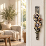 Wildflower Garden Pewter Mezuzah mounted vertically on a pale home doorpost, with yellow and purple flowers with sparkling centers, a small reddish blossom and green curling leaves along a textured silver-toned pewter stem creating a distinctive mezuzah cover that brings its Jewish design and decorative detail into the doorway